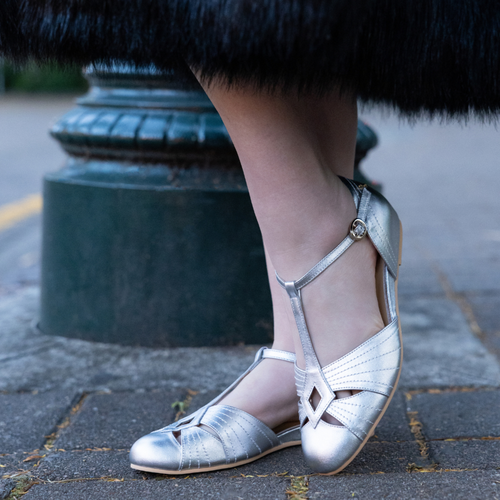 Charlie Stone London silver T-strap flats worn beside a green lamppost